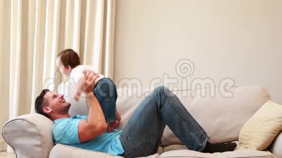 父亲在沙发上和他的孩子玩视频的预览图