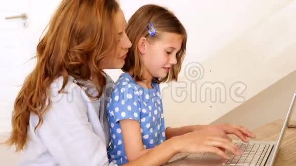 一个小女孩和她的母亲在桌旁用笔记本电脑视频的预览图