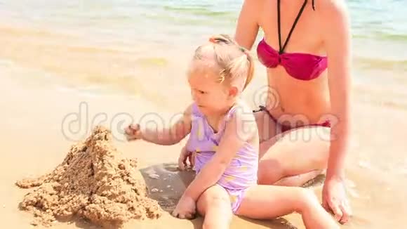母亲小女儿在蔚蓝的海滩上建造沙堡视频的预览图