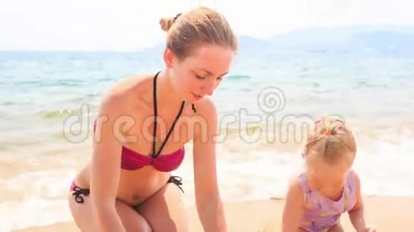 母亲小女儿在蔚蓝的海滩上建造沙堡视频的预览图