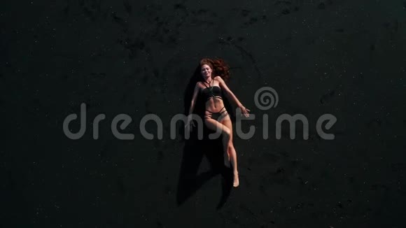 在黑色波光粼粼的沙滩上摆着比基尼的美丽性感女人的顶级鸟瞰图视频的预览图