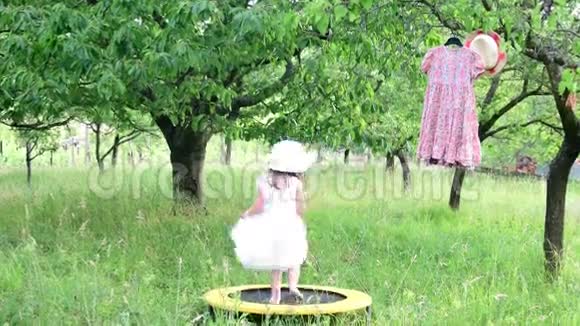 一个可爱的女孩在自然花园里跳舞小女孩在一个小蹦床上跳舞小女孩穿白色婚纱视频的预览图