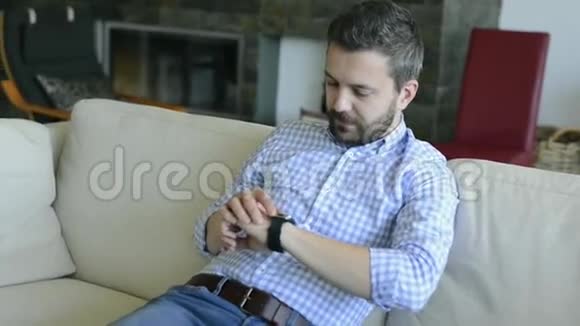 男人坐在沙发上用智能手表视频的预览图