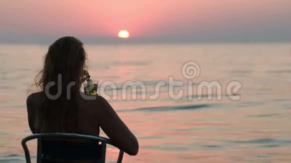 带着鸡尾酒的女人在岸上享受日落视频的预览图