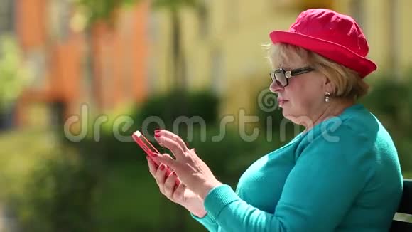 女人坐在长凳上用红色手机视频的预览图