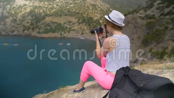 年轻女孩在坐在山上的蓝海附近拍照视频的预览图