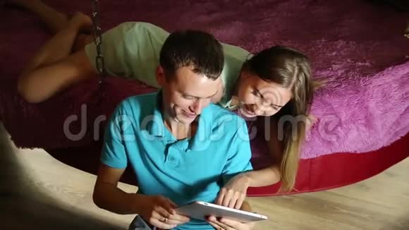 年轻夫妇使用数字平板电脑在线购物一对笑一个女孩躺在家里的床上视频的预览图