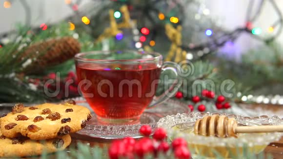 一杯带蜂蜜和饼干的茶雪中圣诞树的一根树枝圣诞灯视频的预览图