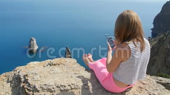 年轻女孩在坐在山上的蓝海附近拍照视频的预览图