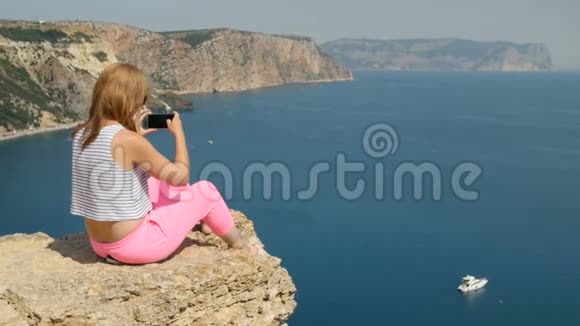 年轻女孩在坐在山上的蓝海附近拍照视频的预览图