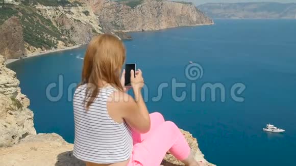 年轻女孩在坐在山上的蓝海附近拍照视频的预览图