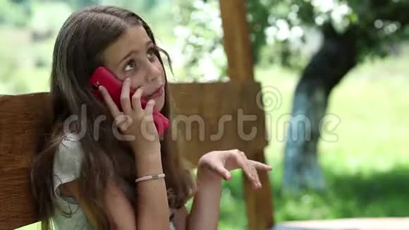 漂亮的女孩带着智能手机坐在花园的长凳上视频的预览图