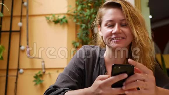 快乐女孩使用智能手机写信息聊天年轻的女人在电话里寻找信息坐在里面视频的预览图