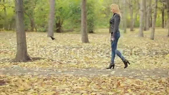 秋天公园里美丽的年轻女子穿皮夹克的金发女郎视频的预览图