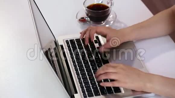 女孩在办公室的笔记本电脑键盘上打字旁边放着茶杯视频的预览图