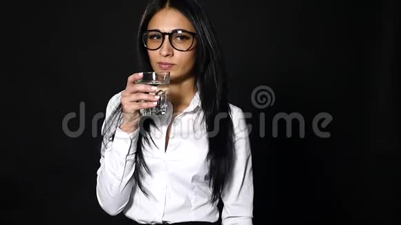 年轻漂亮的女孩在黑色的背景上拿着一杯水视频的预览图