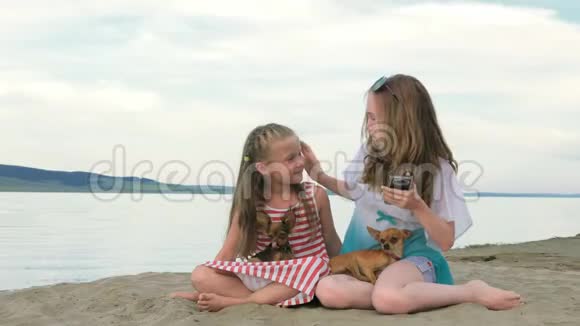 两个十几岁的孩子坐在海滩上打电话视频的预览图