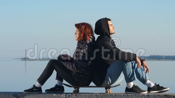 年轻夫妇背靠背坐在滑板上视频的预览图