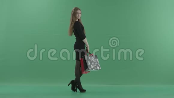 漂亮的女人穿着黑色的小裙子摆着购物袋她正站在一间反对绿色的工作室里视频的预览图