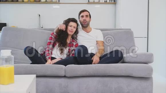 漂亮的女孩和一个年轻人坐在沙发上看电视人们在沙发上放松戴眼镜的年轻人视频的预览图