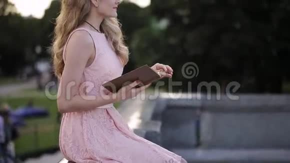 穿着粉红色裙子在公园看书的漂亮女孩视频的预览图