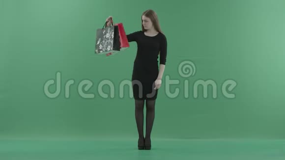漂亮的女人穿着黑色的小裙子摆着购物袋她正站在一间反对绿色的工作室里视频的预览图