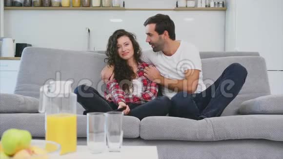 漂亮的女孩和一个年轻人坐在沙发上看电视人们在沙发上放松戴眼镜的年轻人视频的预览图