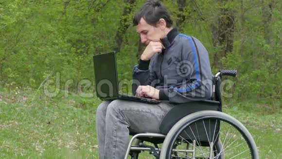残疾人认为轮椅上的笔记本电脑有问题坐在轮椅上在绿色背景下工作视频的预览图
