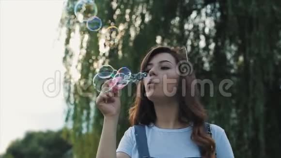 美丽的年轻女子戴着太阳镜在户外吹肥皂泡到处旋转近景慢动作视频的预览图