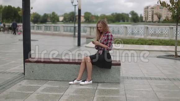 有智能手机的年轻女子坐在公园的长凳上视频的预览图
