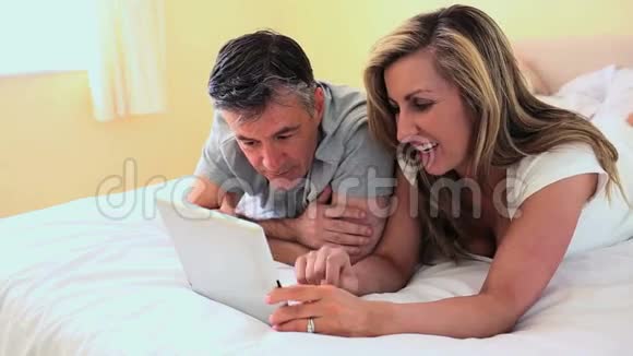 成熟的夫妻躺在床上看着数码平板电脑视频的预览图