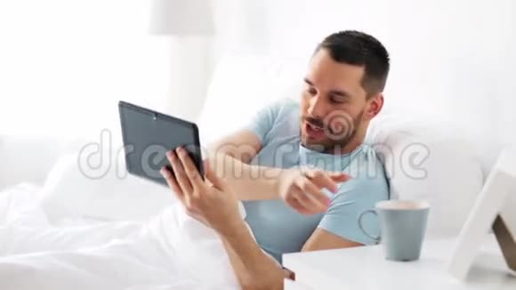 带平板电脑的男人在家里的床上喝咖啡视频的预览图