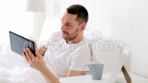 带平板电脑的男人在家里的床上喝咖啡视频的预览图