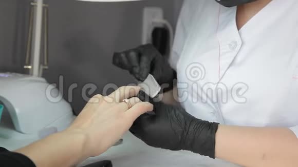 职业美甲师戴着医用黑色面具和黑色手套为女性修指甲视频的预览图