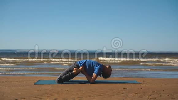 强壮的男人在海滩上练习困难的瑜伽姿势视频的预览图