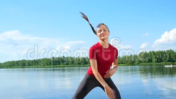 美丽的运动的年轻金发女人做不同的运动湖河蓝天和森林的背景视频的预览图