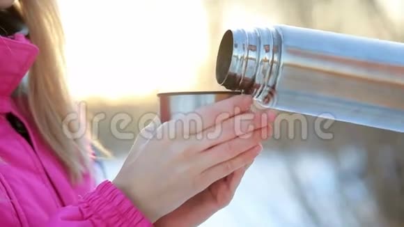 女人手里拿着热水瓶里的杯子在雪白的树枝上喝茶视频的预览图