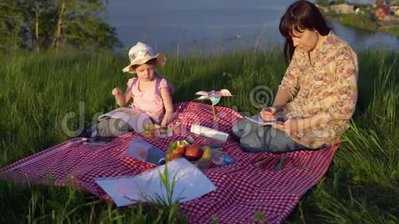 妈妈和女儿在池塘附近的山上野餐视频的预览图