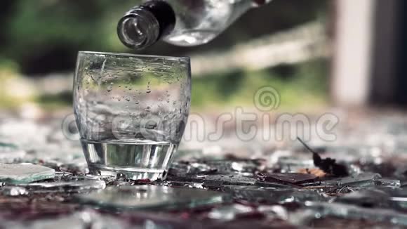 在碎玻璃的背景下将伏特加倒入玻璃杯中视频的预览图