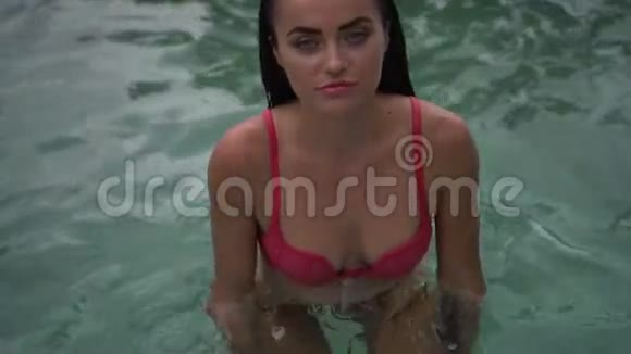 美丽的黑发女人穿着粉红色比基尼在热带度假胜地的室外游泳池放松视频的预览图