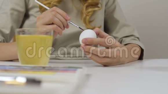 面目全非的女人用刷子涂复活节彩蛋桌子上有一杯水和一碗鸡蛋筹备视频的预览图
