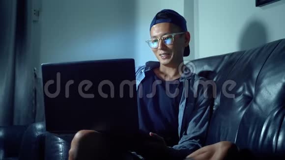 年轻英俊的亚洲男人戴着眼镜用笔记本电脑思考晚上坐在房间里在黑暗中视频的预览图
