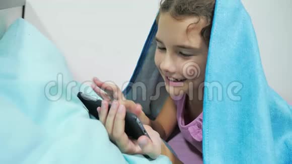 十几岁的女孩在毯子下玩智能手机小女孩睡前躺在床上上网视频的预览图