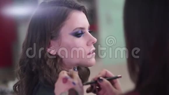 化妆师将化妆应用于一个有吸引力的年轻模特的照片会议LIPS视频的预览图