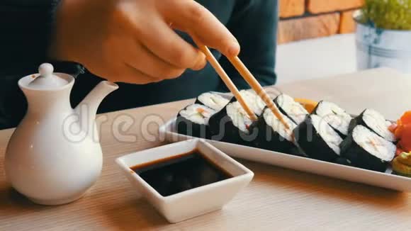一个十几岁的男孩拿着中国竹签的寿司卷把它放进酱油里拿一块粉红色的生姜视频的预览图