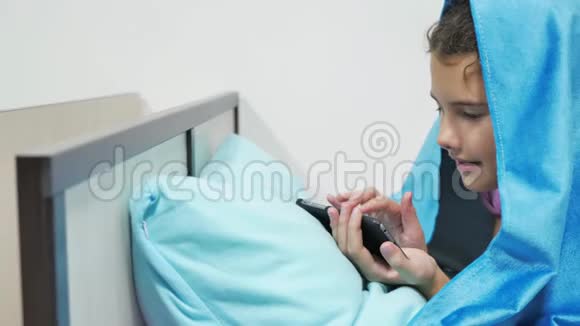 十几岁的女孩在毯子下玩智能手机睡前小女孩躺在床上上网视频的预览图
