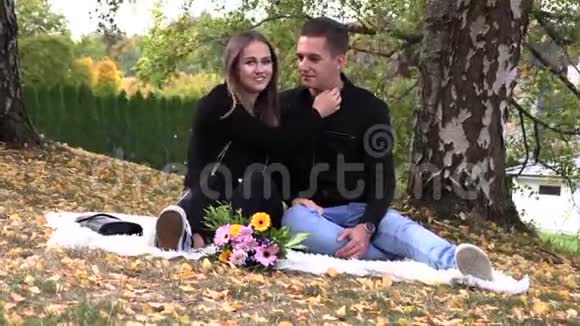 一对年轻夫妇坐在秋天公园的白色床单上视频的预览图