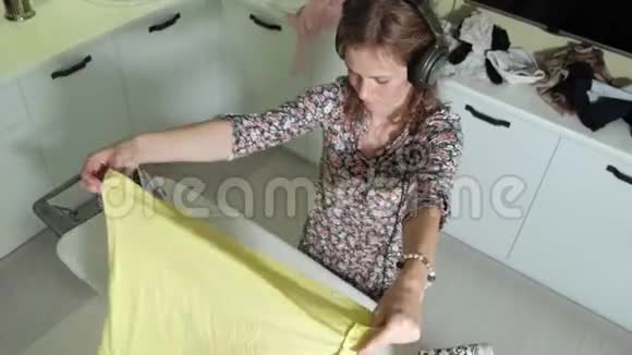 女人在家里熨衣服在厨房里听着耳机上的音乐和跳舞视频的预览图