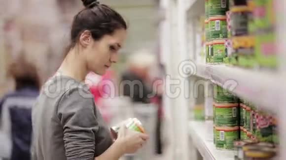 年轻女子在商店里选择罐头食品视频的预览图