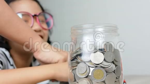 一个亚洲小女孩把硬币放进玻璃罐子里视频的预览图